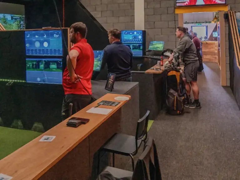 The same unit on Lingfield Way now: golfers across the three simulator bays on a busy night