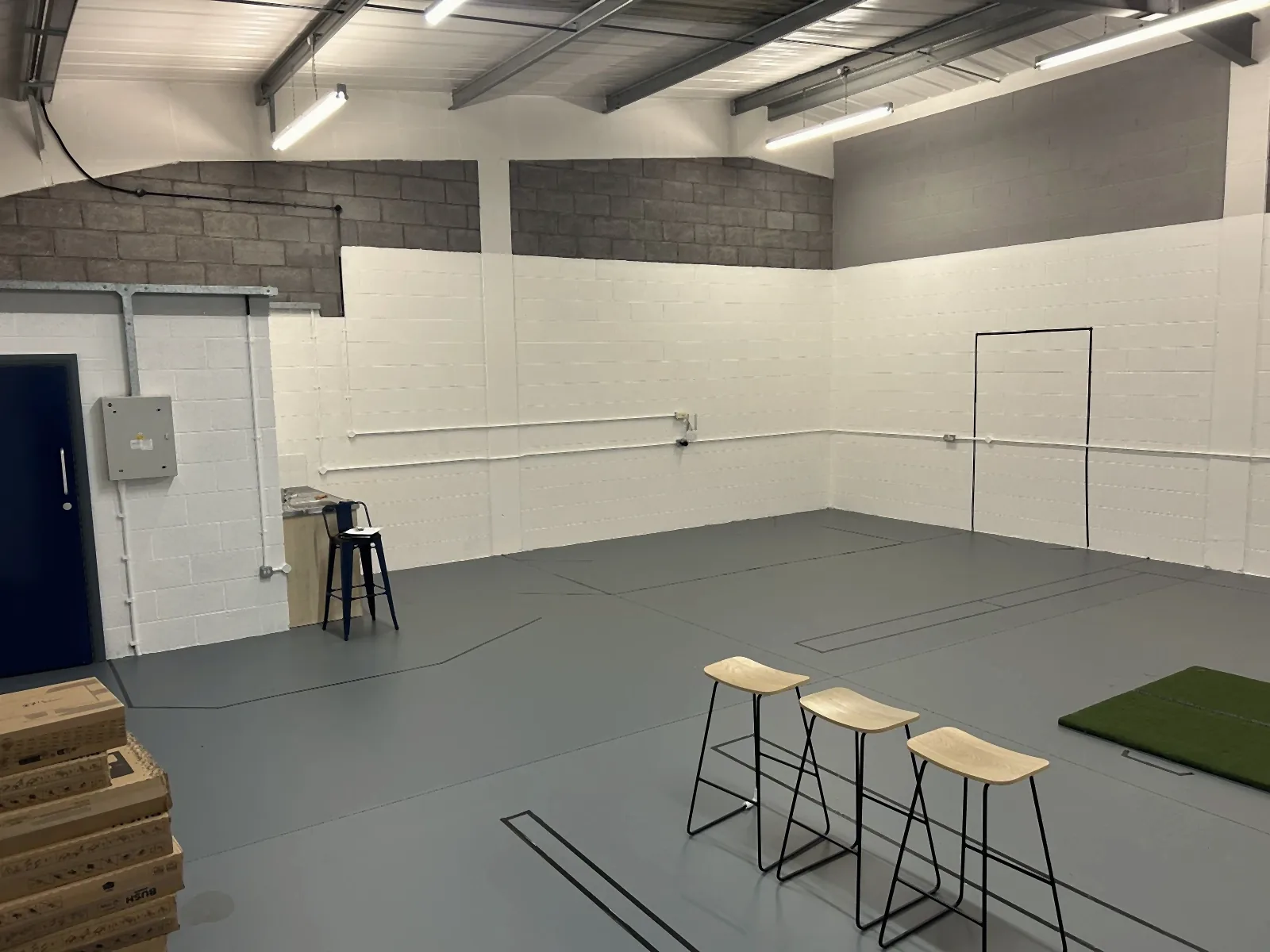 The empty unit on Lingfield Way, Darlington, before Virtual Fairways was fitted out: bare painted blockwork, three stools and a single hitting mat
